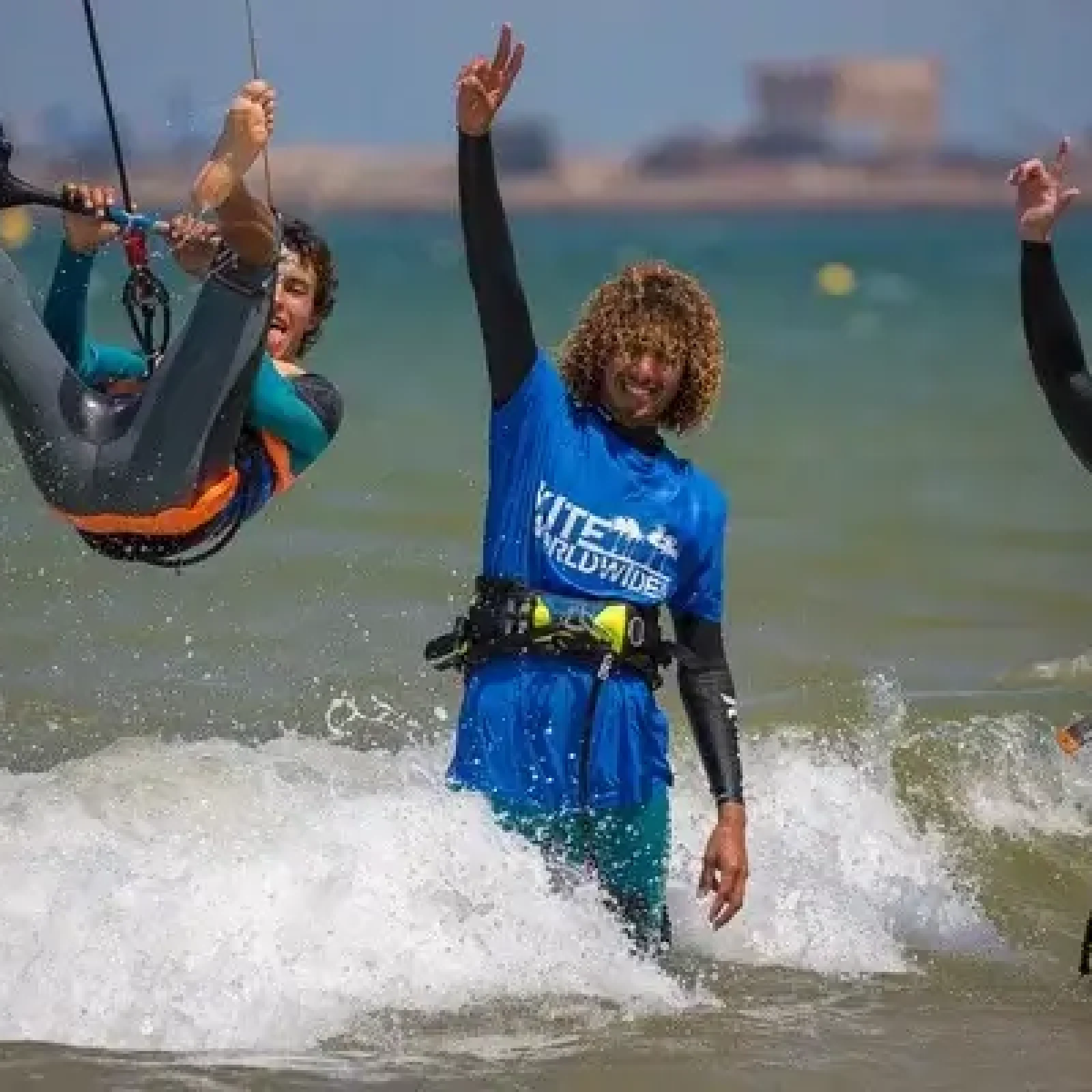 Moniteurs et élève de kitesurf pratiquent dans des vagues côtières peu profondes près d'Essaouira avec bâtiments visibles à l'intérieur des terres