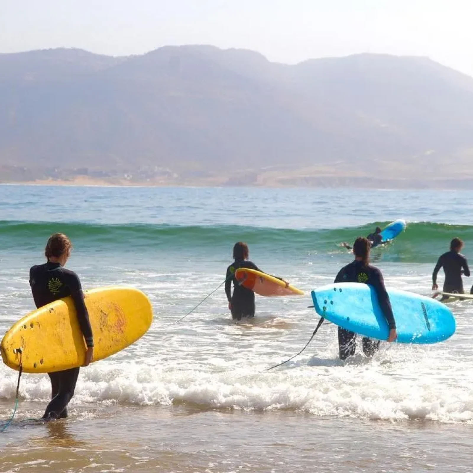 Gruppe von Surfern in Neoprenanzügen tragen farbenfrohe Surfbretter ins Wasser an einem Küstenstrand.