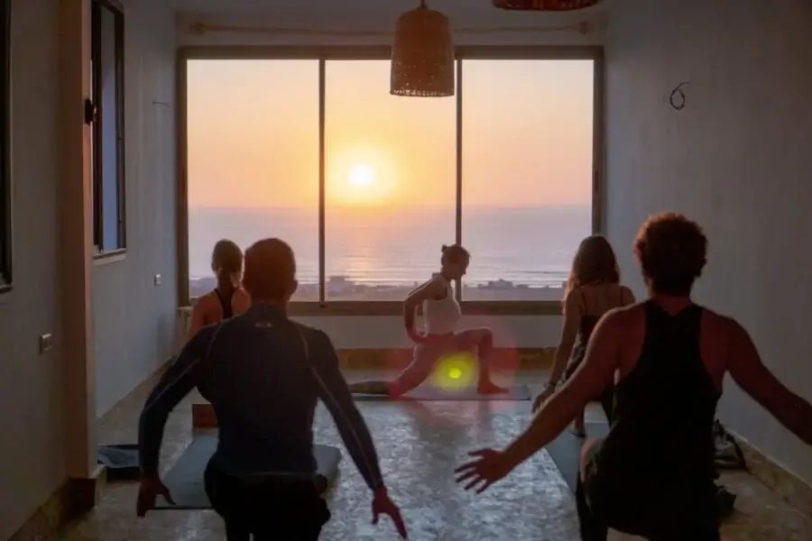 Group yoga class with ocean and sunset visible through large windows in the studio at Blue Mind Morocco.