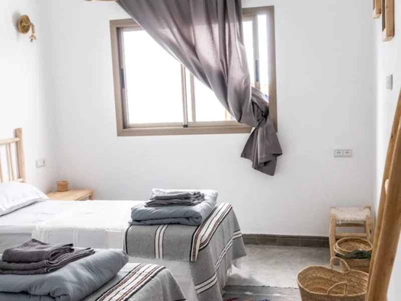Twin bedroom with two beds, woven ceiling lamp, gray curtains at window, and wooden furnishings in minimalist decor.
