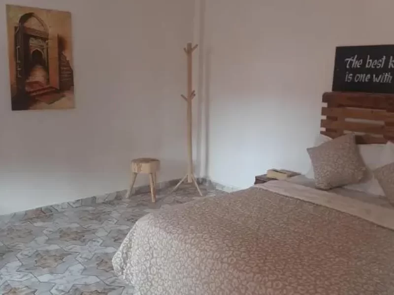 Chambre Suite Famille à Imsouane Soul Lodge avec lit, portemanteau en bois et œuvre d'art murale.