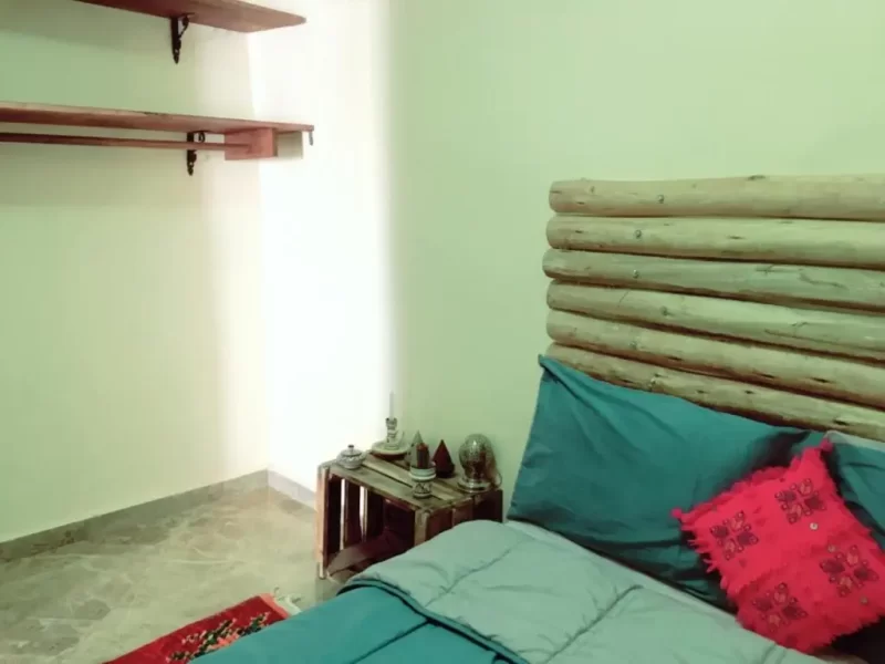 Une chambre à Imsouane Soul Lodge présente un lit double avec tête de lit sarcelle et accents rouges, étagères en bois et murs vert pâle.