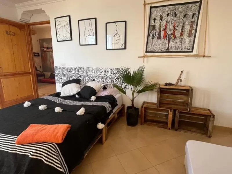 Double bedroom at Kosa Surf Camp in Taghazout with black bedding, patterned headboard, and framed wall art.