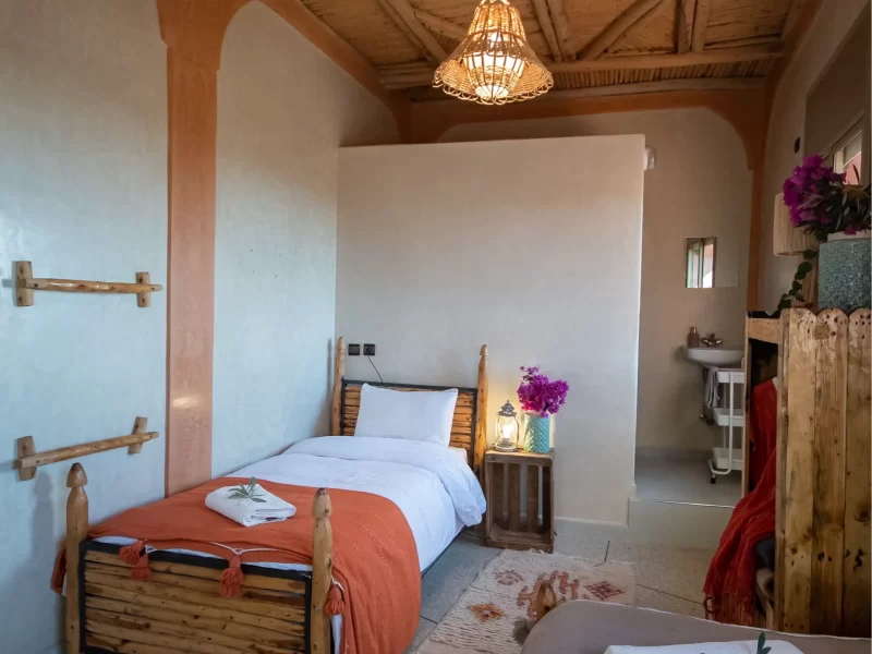 Chambre à lits jumeaux partagée à Tamazirt by Amayour à Taghazout avec lits en bois, plaid orange et suspension tissée.