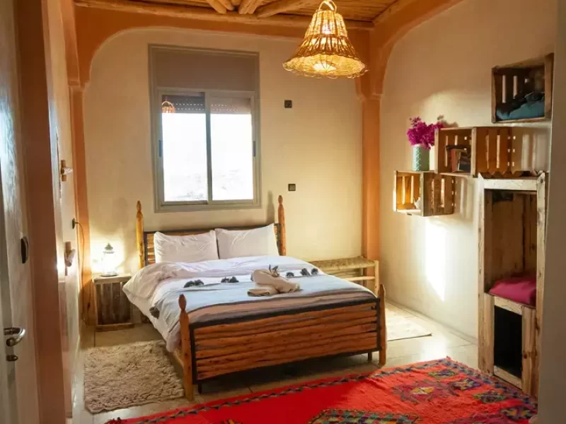 Grande chambre Double à Tamazirt by Amayour avec architecture en bois, suspension décorative et tapis traditionnels rouges.
