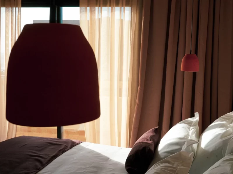 Dreibettzimmer mit weißen Kissen, dunkler Bettwäsche, braunen Vorhängen und Hängelampe im L'Oued the Lodge.