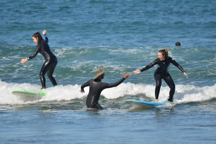Group surf lesson at Plage Oudaya showing instructor guiding students in the water with waves in background.