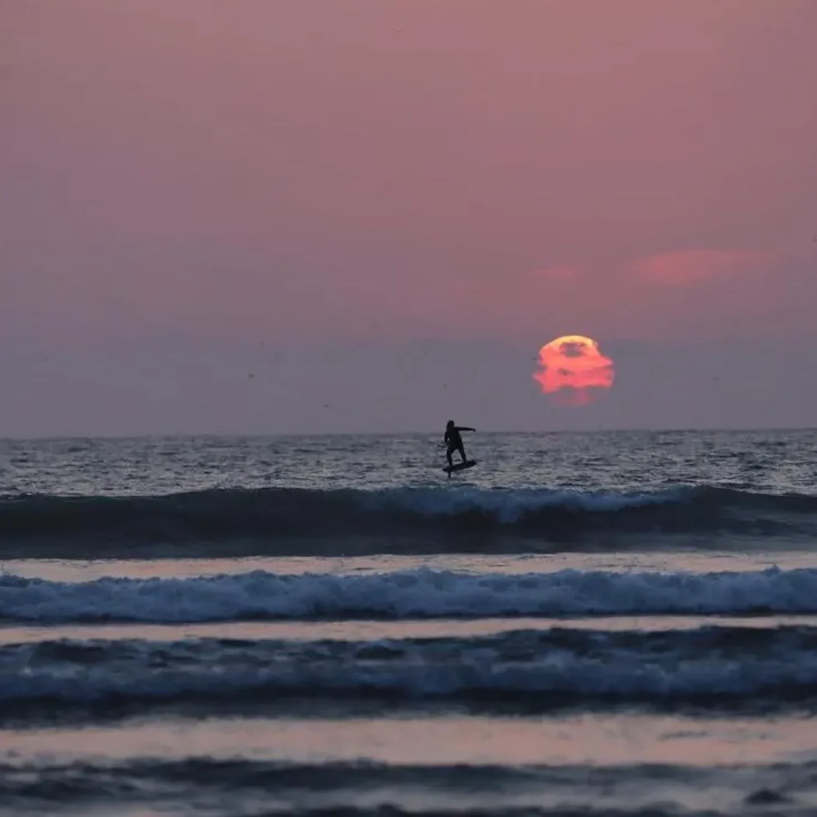 Un kitesurfeur est visible dans l'eau à Essaouira au coucher du soleil avec un grand soleil rougeoyant à l'horizon.