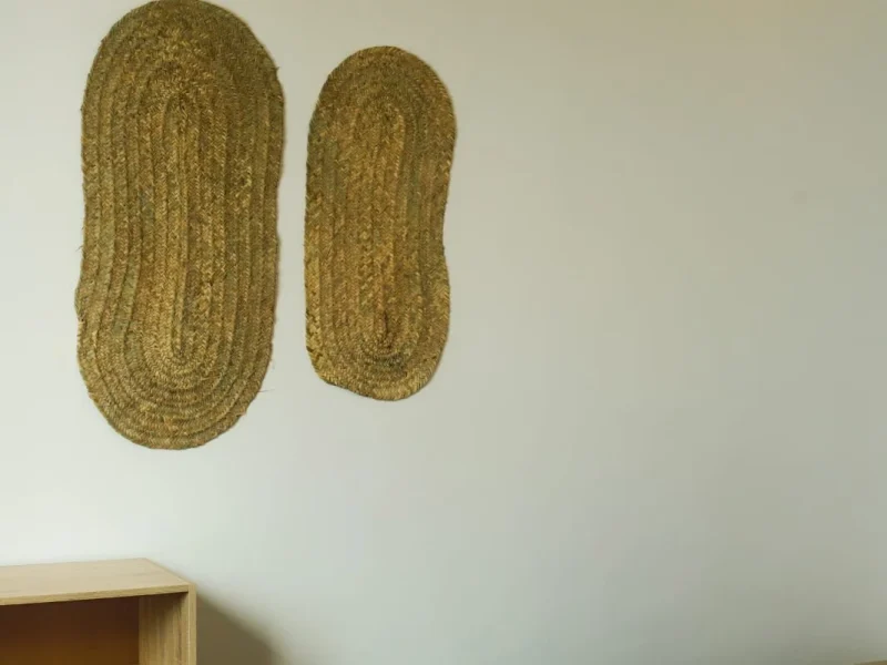 Double room interior with two oval woven natural fiber wall hangings mounted on pale wall.