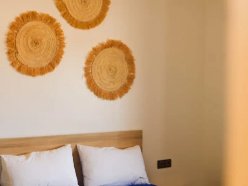 Triple room bed with white pillows, blue blanket, and woven circular wall decorations above headboard.