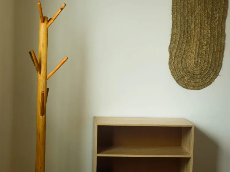 Private room features wooden coat stand with pegs and three-shelf open storage unit on neutral wall.