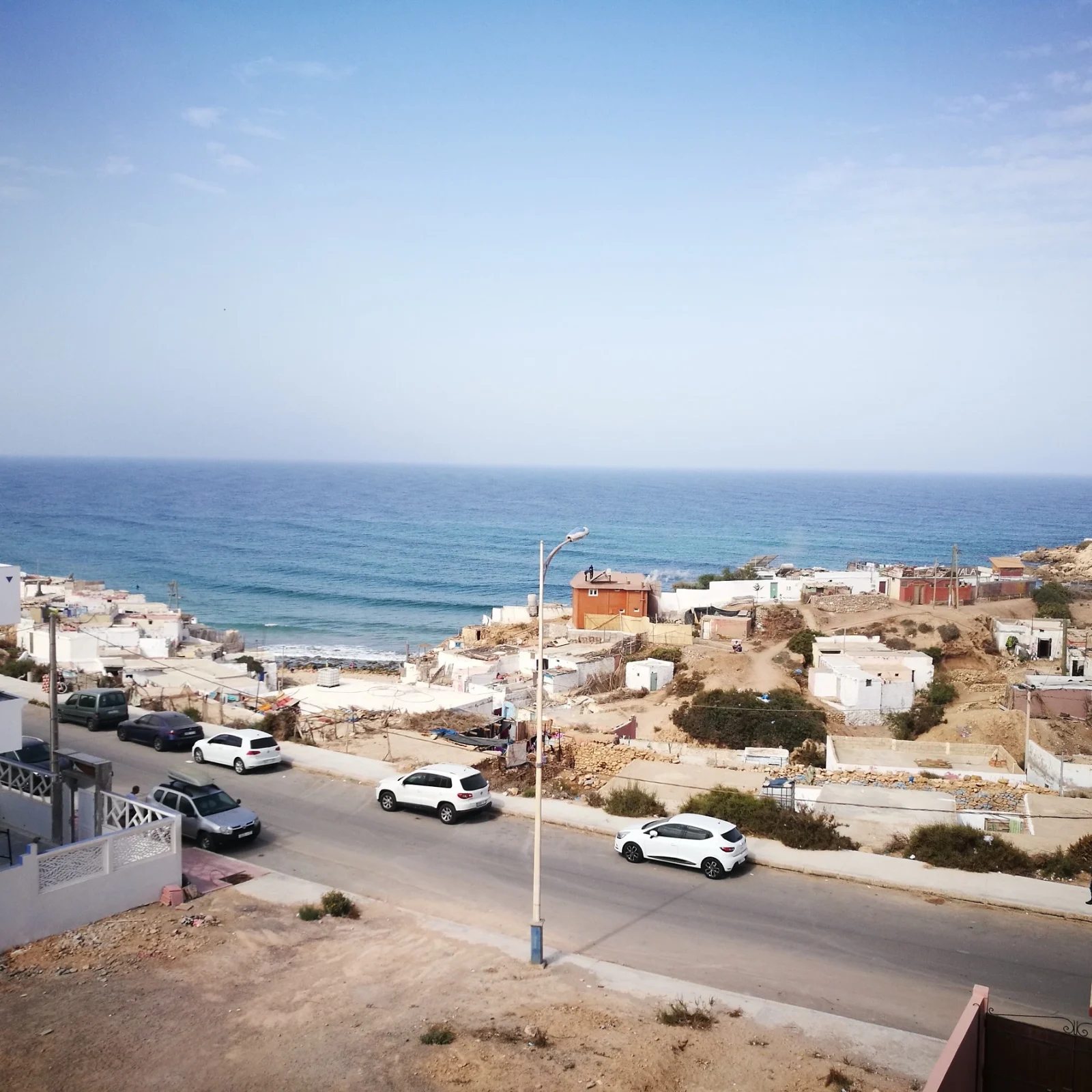 Vue surélevée du village d'Imsouane montrant plage, océan, bâtiments résidentiels et voitures garées le long du littoral.
