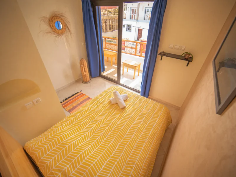 Double bedroom with yellow patterned bedspread and glass doors opening to a terrace overlooking the village of Imsouane.