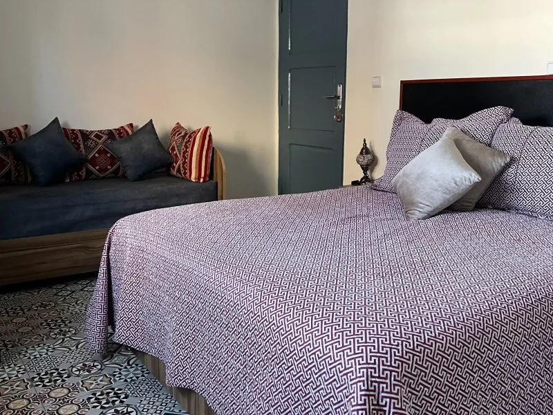Intérieur de chambre Double à Villa Idyssa avec linge à motifs, assise canapé et carrelage de style marocain au sol.