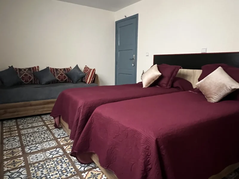 Chambre privée à Villa Idyssa à Imsouane présente un lit double avec linge bordeaux, carrelage de sol géométrique et coin assise avec oreillers décoratifs.