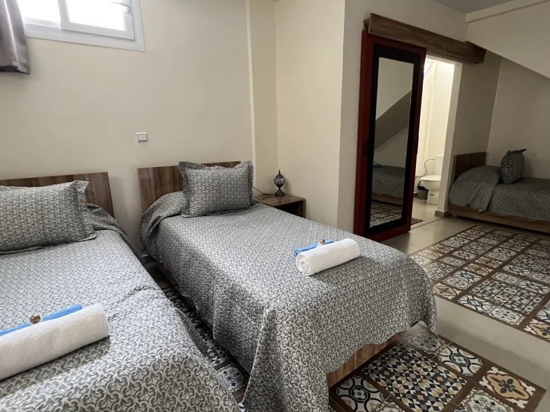 Une chambre partagée à Villa Idyssa présente trois lits simples avec linge gris à motifs, tables de chevet en bois et tapis à motifs géométriques.