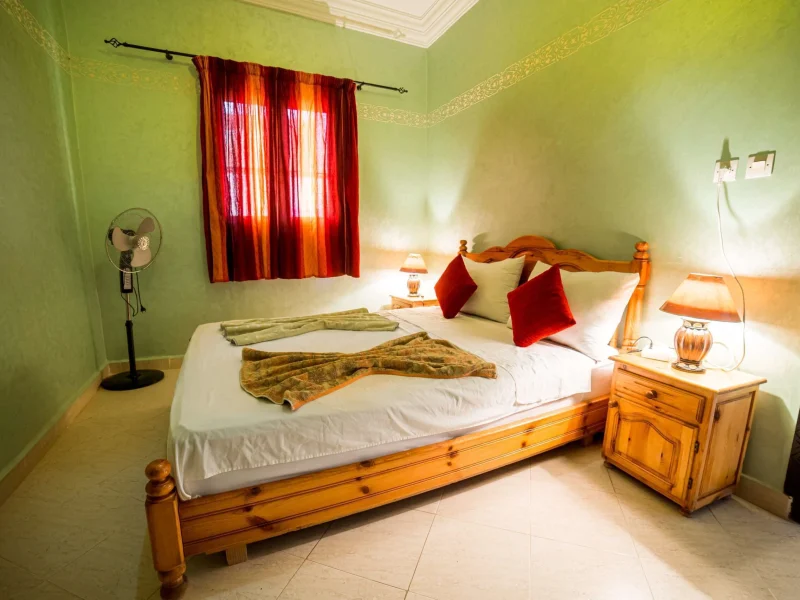 Double bedroom in Taghazout with wooden bed, lime green walls, and red curtains.