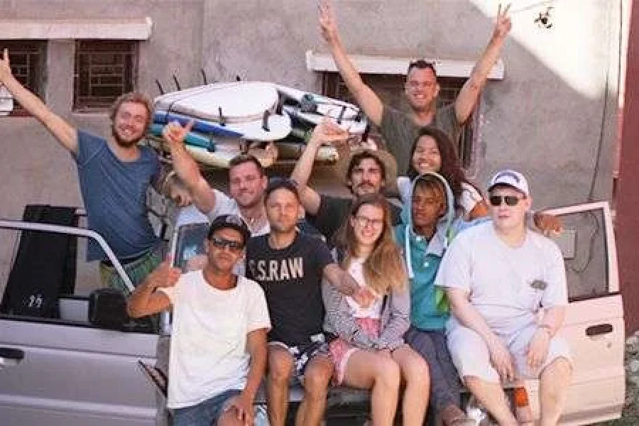 Group of approximately 13 people posing with surfboards outside Original Surf Morocco camp in Taghazout village.
