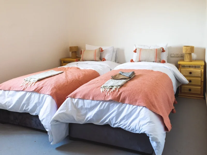Twin beds with white linens and coral blankets at Surf Les Vagues hotel in Essaouira.