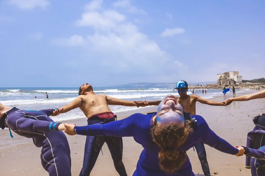 Gruppe von Surfern in Neoprenanzügen macht Dehnübungen im Sand am Strand von Sidi Kaouki.