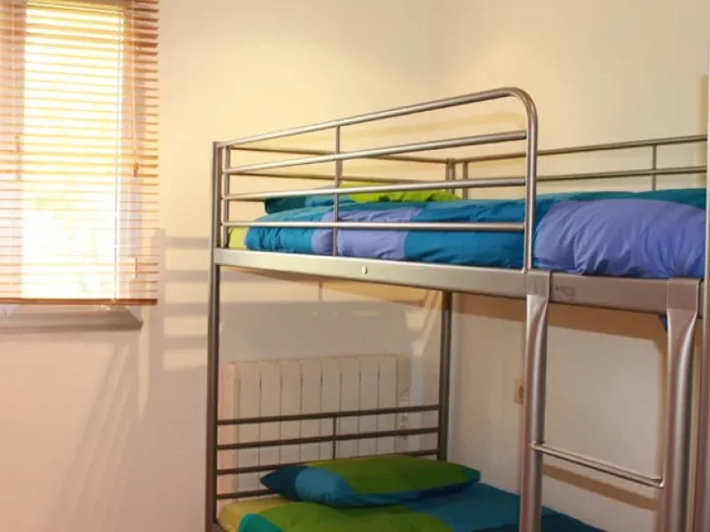 Metall-Etagenbetten mit bunter blauer und grüner Bettwäsche in einem Gemeinschafts-Unterkunftszimmer im Alawa Pantin.