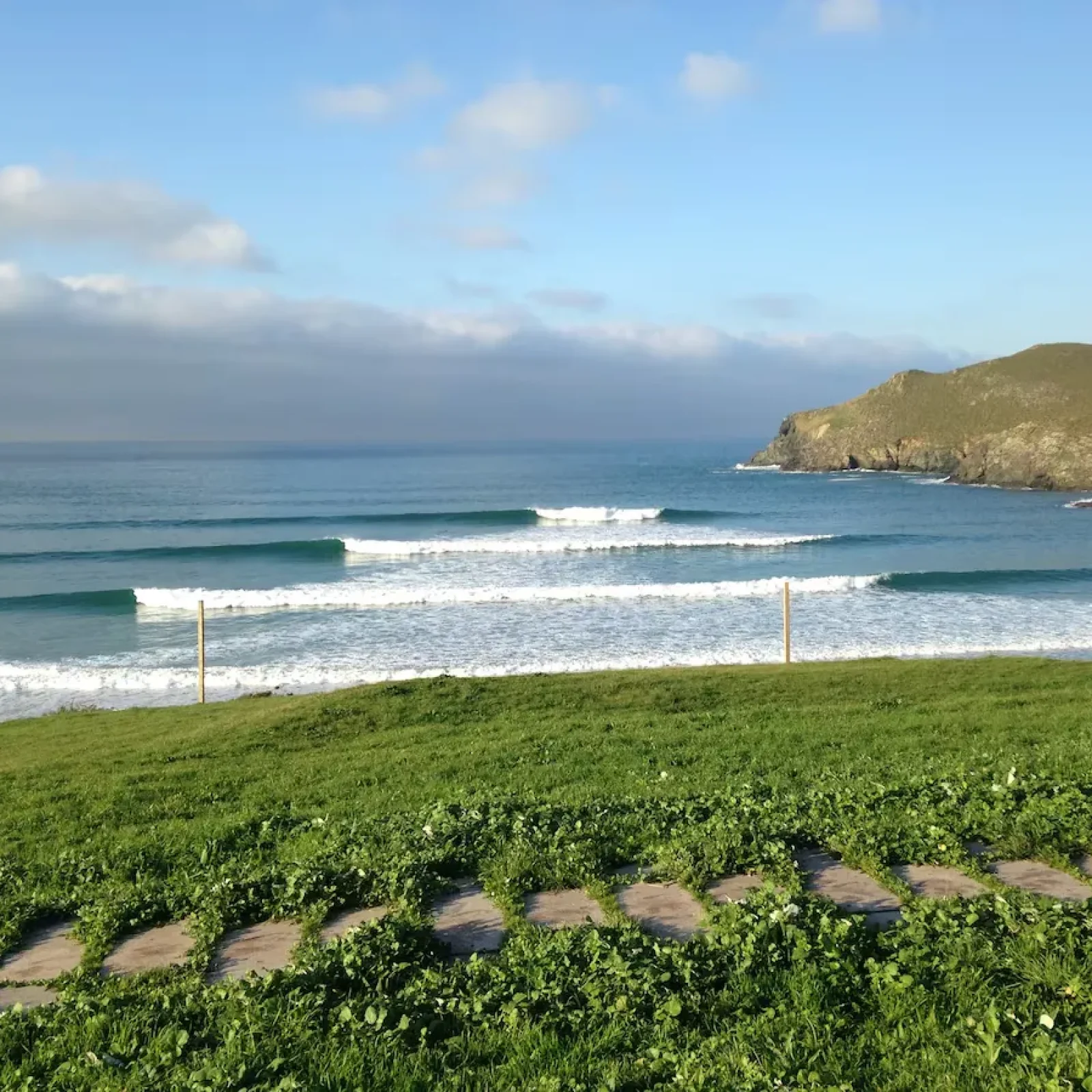 Pantin-Surfstrand in Galicien mit mehreren Wellenlinien und grasiger Küstenlinie mit Blick auf felsige Klippen.