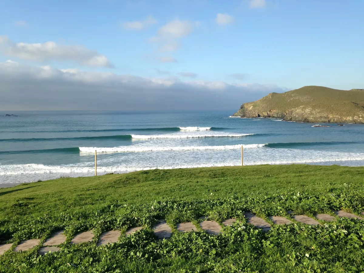 Pantin surf beach in Galicia with multiple wave lines and grassy coastline overlooking rocky cliffs.