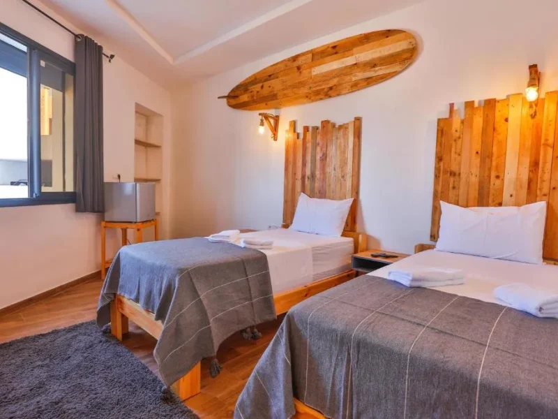 Zwillingszimmer im Moon Surf House mit Holzbettrahmen mit weißer Bettwäsche und einem dekorativen Holzsurfbrett an der Decke montiert.