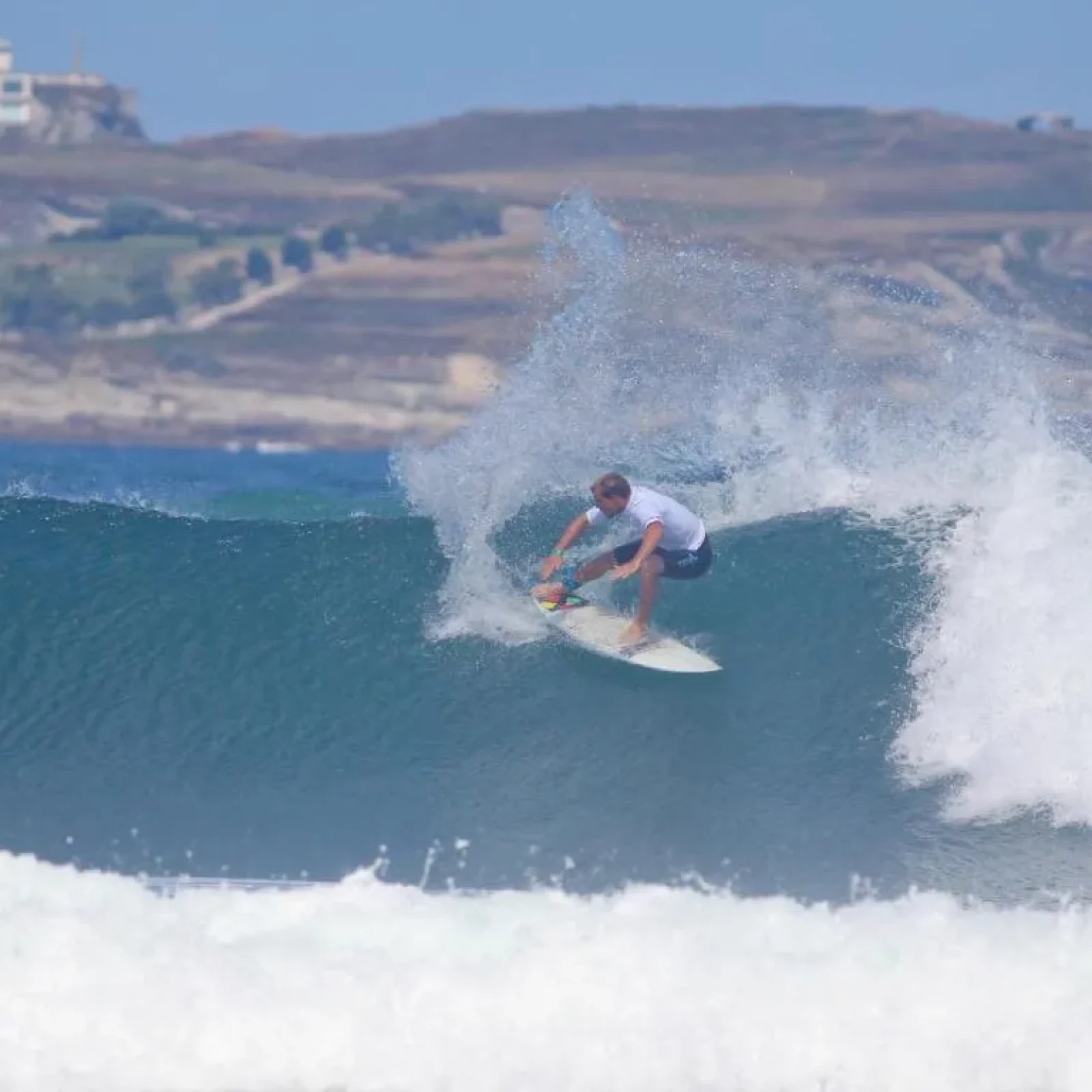 Surfer reitet eine Welle in Cantabria, Spanien, mit Küstenlandschaft und Hang im Hintergrund sichtbar.