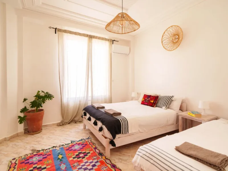 Family room bedroom with white bedding, woven pendant lamp, and decorative colorful rugs at Sunshine Surf Morocco.