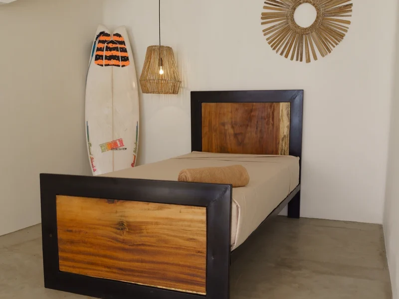 Gemeinschaftsschlafzimmer im Laola Surf Camp mit Bett mit holzgerahmtem Kopfteil und einem dekorativen Surfbrett mit orangem und marineblauem Grafik-Design an der Wand montiert.