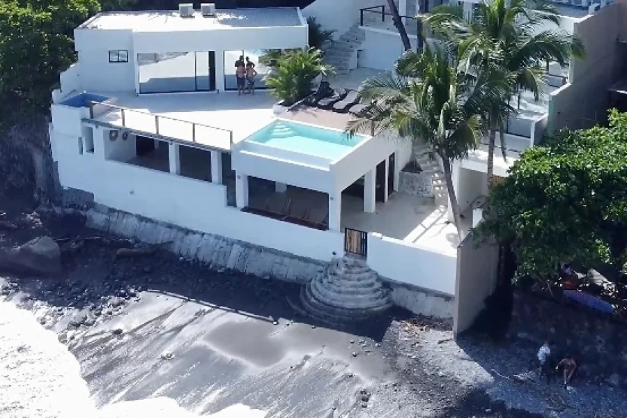 Établissement moderne blanc en bord de mer avec piscine turquoise et plusieurs terrasses surplombant la plage El Sunzal au Salvador.