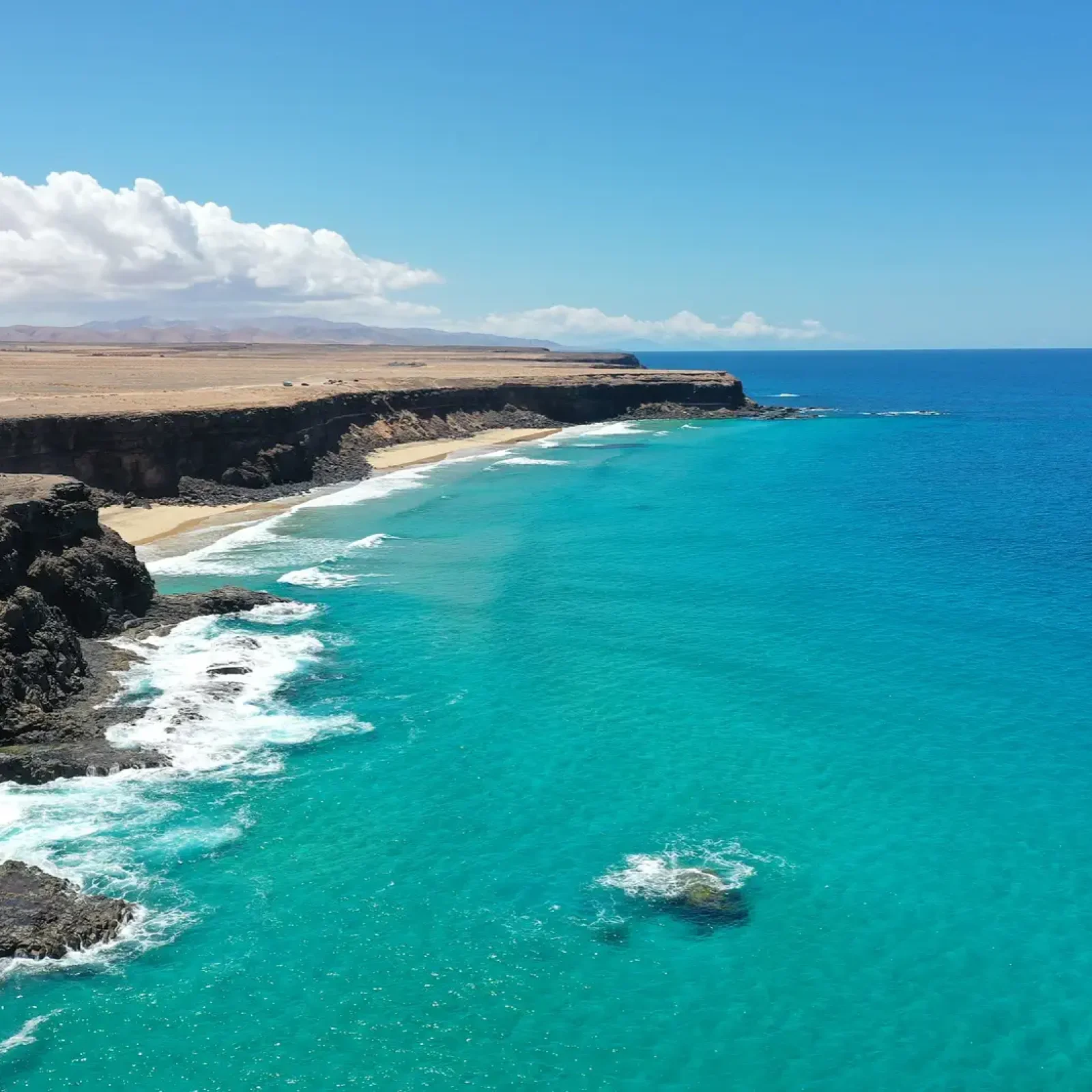 Falaises volcaniques noires avec crique de plage de sable et eaux atlantiques turquoise au large de la côte nord de Fuerteventura.
