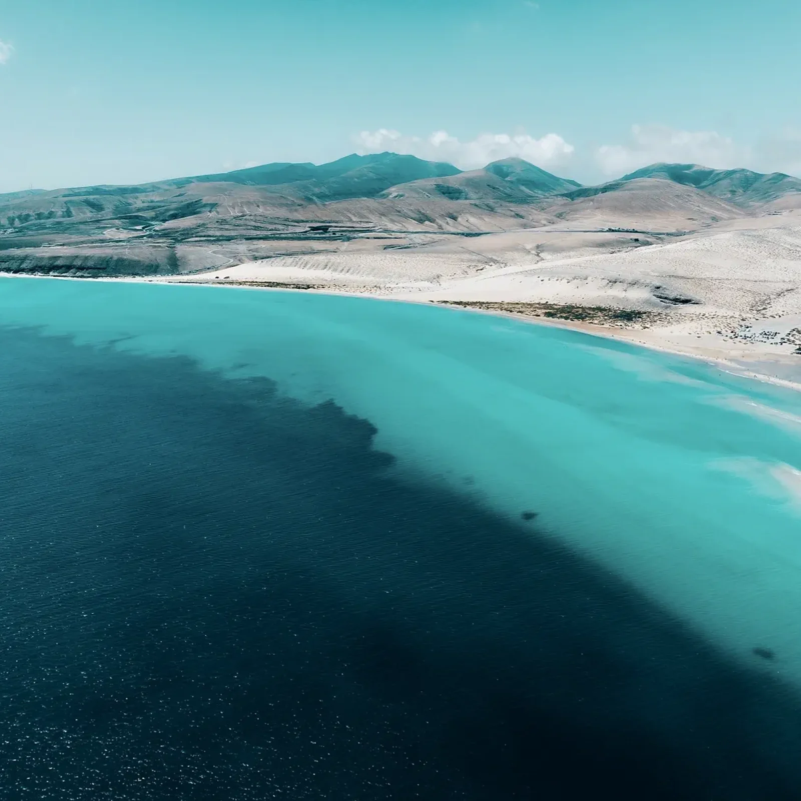 Vue aérienne des eaux de baie turquoise avec plage de sable blanc et montagnes volcaniques en arrière-plan près de Fuerteventura, îles Canaries