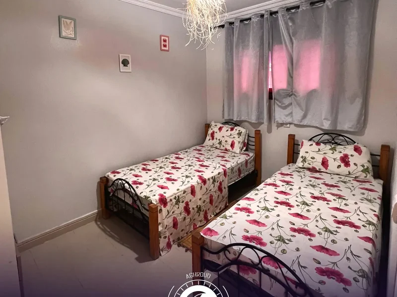 Habitación compartida con dos camas individuales con ropa de cama floral estampada en Purple House Surf Camp en Taghazout.