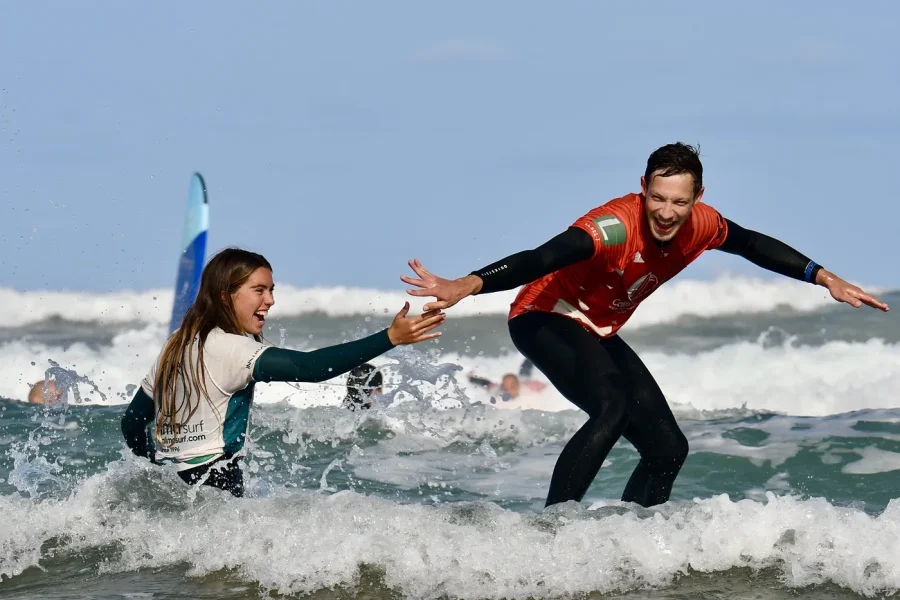 Istruttore di surf in giacca rossa aiuta una giovane studentessa in acque basse durante una lezione alla spiaggia di Famara, Lanzarote.
