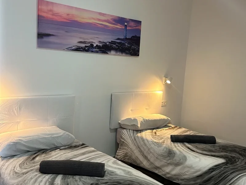 Twin bedroom featuring two single beds with striped black and white bedding, white headboards, and a lighthouse sunset canvas on the wall above.