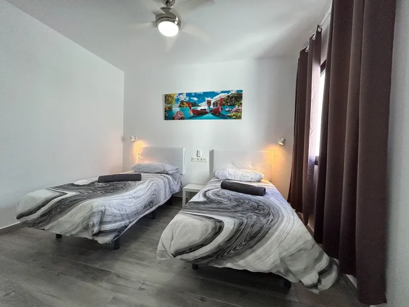 Twin room at Calima Famara with two single beds, warm reading lights, and tropical island artwork above headboard.