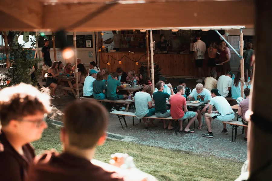 Eine Gästegruppe versammelt sich unter einer überdachten Außenterrasse im Surfcamp Zarautz zu einem Abendessen und einer Zusammenkunft.