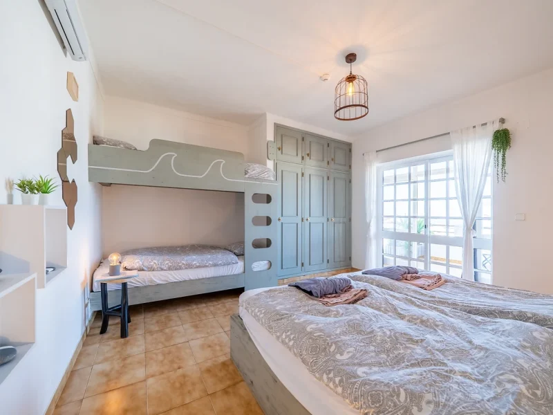 Four Deluxe room features a queen bed in foreground and gray bunk beds on left wall with wave motif detail.