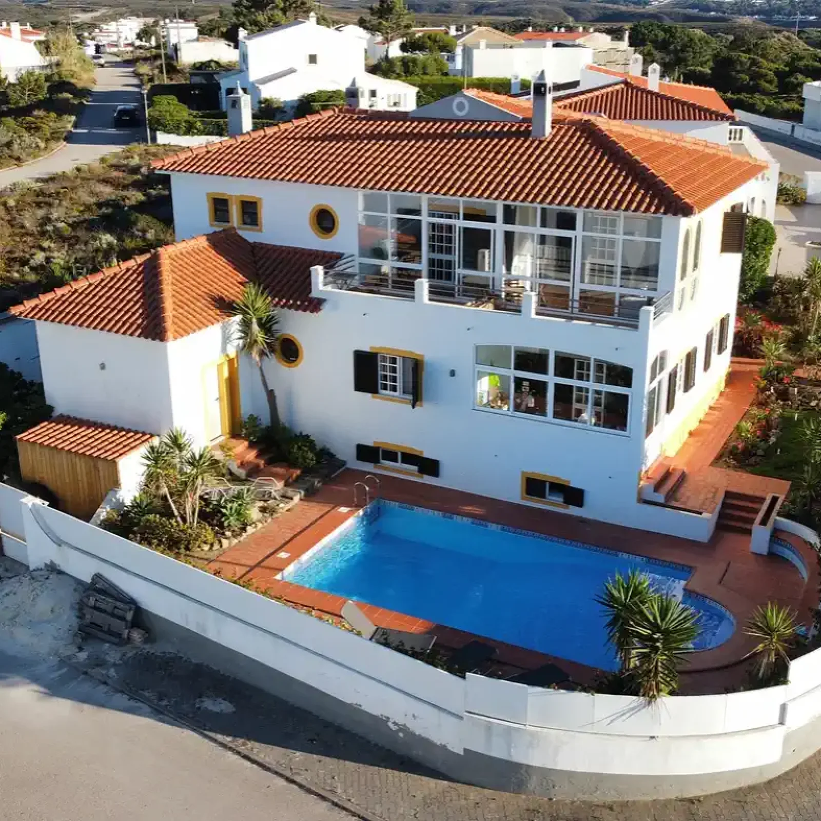 Vue aérienne de l'hébergement SURFinn Algarve avec piscine bleue, architecture blanche et terracotta dans le paysage rural portugais.