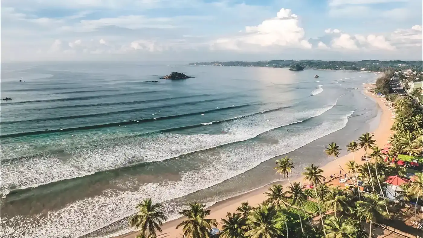 Ahangama beach showing consistent wave breaks, sandy shoreline, and forested coastline at sunrise on Sri Lanka south coast