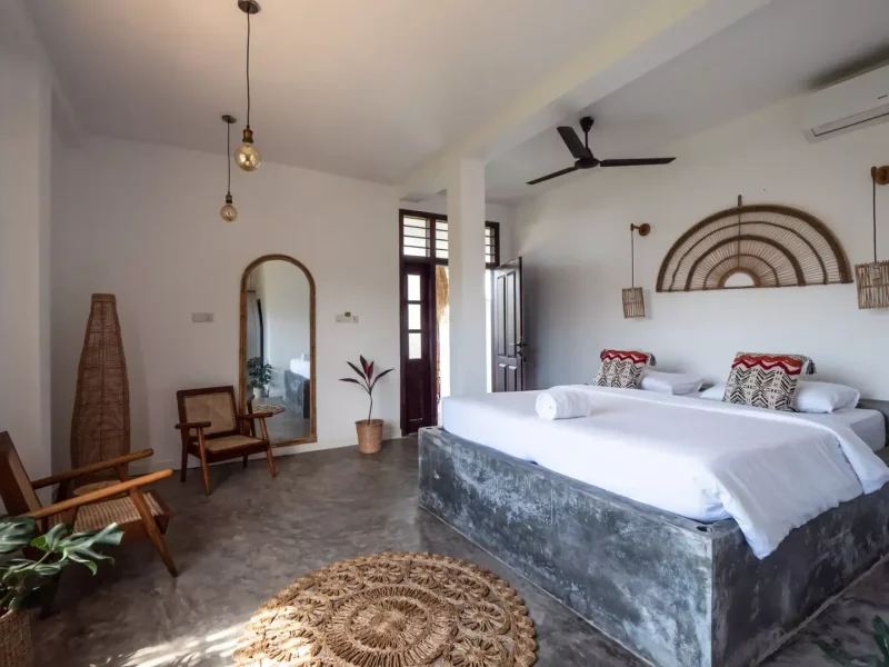 Habitación Superior Ensuite en Kabalana Beach con cama plataforma con ropa blanca, espejo en arco, decoración mural de rattan e iluminación contemporánea.