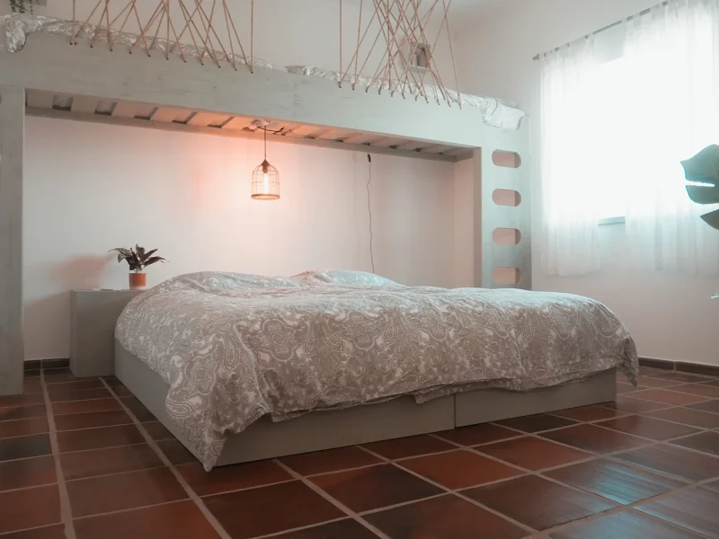 Bedroom interior featuring a queen bed with patterned bedding, pendant lamp, and minimalist decor at SURFinn Algarve.