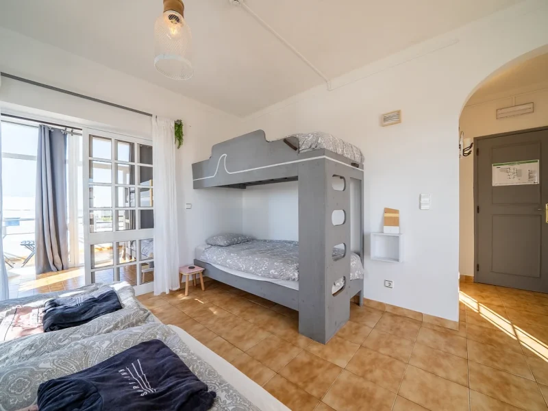 SURFinn Algarve's Six Deluxe room features a gray bunk bed with wave motif and a single bed, with terrace access visible.