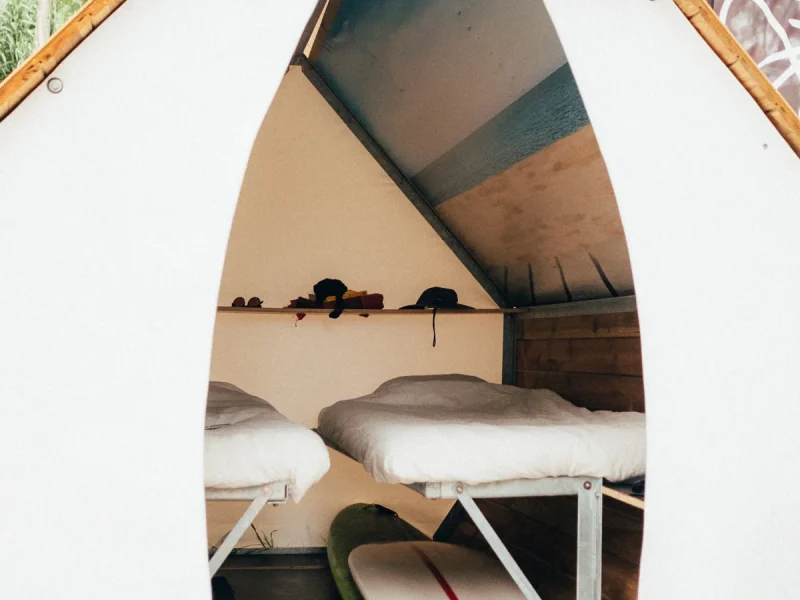 Interno della camera Sheddie Deluxe al Surfcamp Zarautz con letti gemelli con lenzuola bianche e tavole da surf riposte.