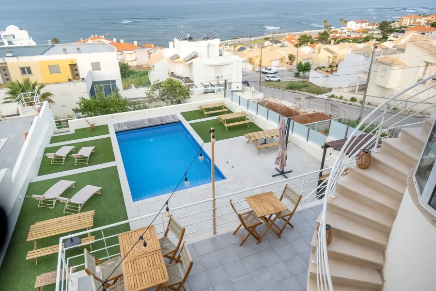 Azotea de SURFinn Figueira da Foz con piscina azul brillante, tumbonas de madera y vistas hacia el litoral y los edificios residenciales cercanos.