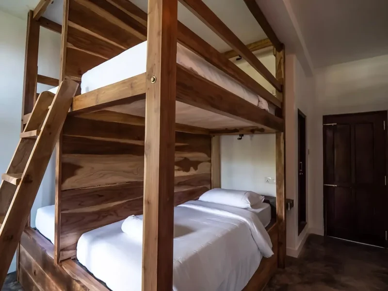 Habitación de dorm compartido con literas apiladas de madera y ropa blanca en Surf Camp Ahangama, Sri Lanka.
