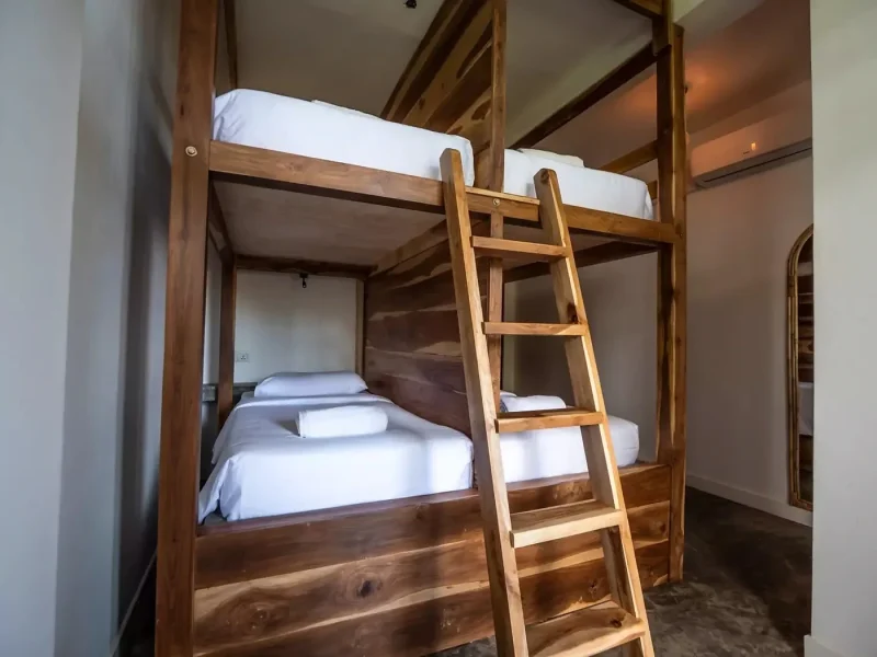 Habitación de alojamiento compartido en el camp de Ahangama con dos estructuras de litera de madera, ropa blanca y escalera de acceso de madera.