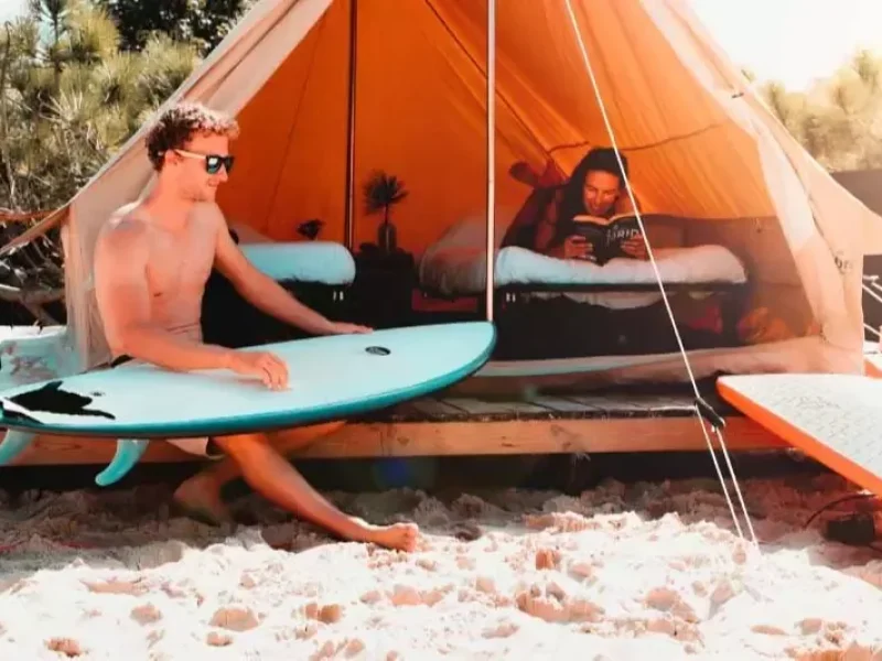 Due persone dentro e fuori una tenda in canvas arancione su una spiaggia con tavole da surf vicino nel Paese Basco, Spagna.